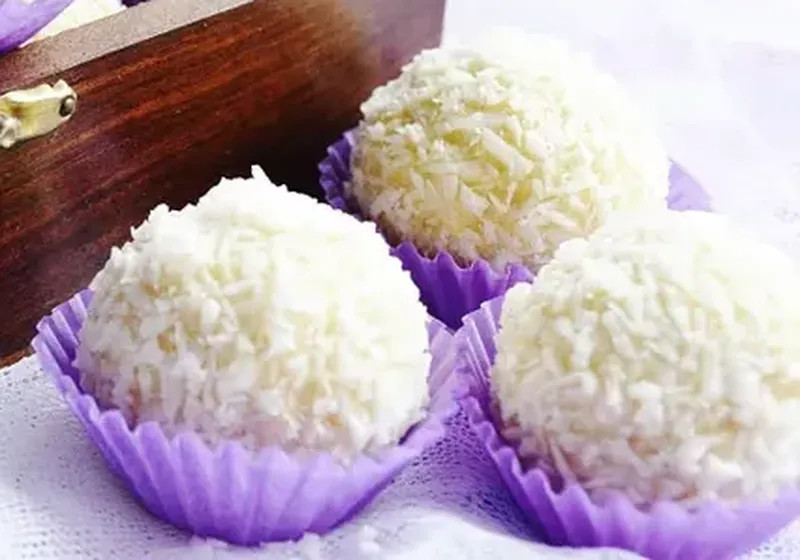 Domácí vánoční cukroví kokosové kuličky Raffaello ve fialových papírových košíčcích.